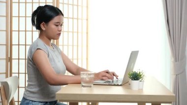 Evde oturan Asyalı bir kadın bilgisayarını kullanarak gelirini ve harcamalarını kaydediyor. Düzenli ve finansal olarak bilinçli kalıyor..