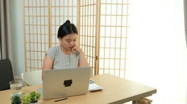 Evde oturan Asyalı bir kadın bilgisayarını kullanarak gelirini ve harcamalarını kaydediyor. Düzenli ve finansal olarak bilinçli kalıyor..