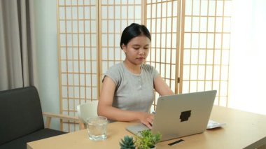 Evde oturan Asyalı bir kadın bilgisayarını kullanarak gelirini ve harcamalarını kaydediyor. Düzenli ve finansal olarak bilinçli kalıyor..