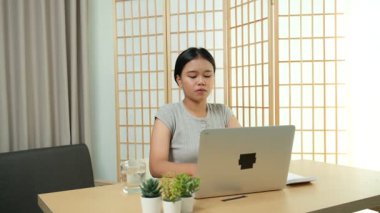 Evde oturan Asyalı bir kadın bilgisayarını kullanarak gelirini ve harcamalarını kaydediyor. Düzenli ve finansal olarak bilinçli kalıyor..