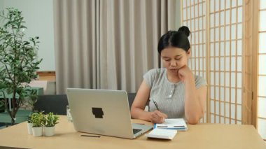 Evde oturan Asyalı bir kadın bilgisayarını kullanarak gelirini ve harcamalarını kaydediyor. Düzenli ve finansal olarak bilinçli kalıyor..