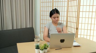 Evde oturan Asyalı bir kadın bilgisayarını kullanarak gelirini ve harcamalarını kaydediyor. Düzenli ve finansal olarak bilinçli kalıyor..