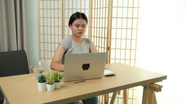 Evde oturan Asyalı bir kadın bilgisayarını kullanarak gelirini ve harcamalarını kaydediyor. Düzenli ve finansal olarak bilinçli kalıyor..