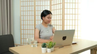 Evde oturan Asyalı bir kadın bilgisayarını kullanarak gelirini ve harcamalarını kaydediyor. Düzenli ve finansal olarak bilinçli kalıyor..