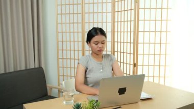 Evde oturan Asyalı bir kadın bilgisayarını kullanarak gelirini ve harcamalarını kaydediyor. Düzenli ve finansal olarak bilinçli kalıyor..