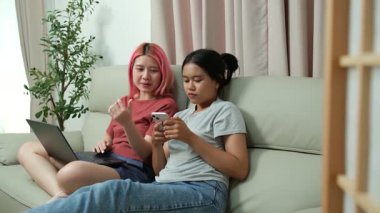 İki kız kardeş boş zamanlarını en sevdikleri kanepede rahat ve eğlenceli bir ortamda dizüstü bilgisayarlarıyla ve akıllı telefonlarıyla oynayarak geçirirler..