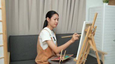 Sevimli genç kız evde resim çizerek ve boyayarak en sevdiği aktiviteyle yaratıcılığını ifade ediyor. Çocukluk hayal gücü, sanat ve oyun yoluyla öğrenme kavramı.