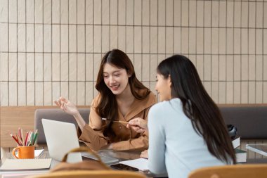 Parlak bir çalışma ortamında, iki arkadaş laptoplarını ve notlarını kullanarak derin akademik konuşmaları teşvik etmek için birlikte beyin fırtınası yaparlar..