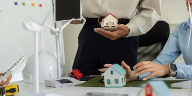 Çeşitli bir ekip, gelecekteki sürdürülebilirlik sorunlarına odaklanan stratejik planlama toplantısında yenilenebilir enerji sergileyen yenilikçi konut modellerini tartışıyor ve değerlendiriyor..