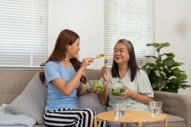 Sıcak bir ortamda, bir anne ve kızı salatalarının tadını çıkarırken kahkahalarını paylaşıyor, sağlıklı yemek ve aile geçimini özetliyor..