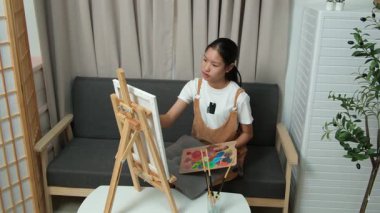 Sevimli genç kız evde resim çizerek ve boyayarak en sevdiği aktiviteyle yaratıcılığını ifade ediyor. Çocukluk hayal gücü, sanat ve oyun yoluyla öğrenme kavramı.