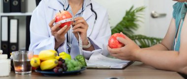 Konsültasyon sırasında, beslenme uzmanı elmayı porsiyonları tartışmak için ölçerek, beslenme için kapsamlı bir yaklaşımı destekleyici bir ortamda göstermektedir..