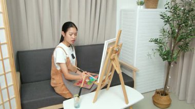 Sevimli genç kız evde resim çizerek ve boyayarak en sevdiği aktiviteyle yaratıcılığını ifade ediyor. Çocukluk hayal gücü, sanat ve oyun yoluyla öğrenme kavramı.