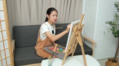 Sevimli genç kız evde resim çizerek ve boyayarak en sevdiği aktiviteyle yaratıcılığını ifade ediyor. Çocukluk hayal gücü, sanat ve oyun yoluyla öğrenme kavramı.