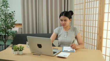 Evde oturan Asyalı bir kadın bilgisayarını kullanarak gelirini ve harcamalarını kaydediyor. Düzenli ve finansal olarak bilinçli kalıyor..