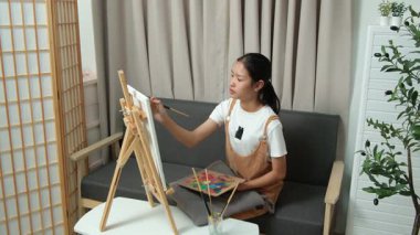 Sevimli genç kız evde resim çizerek ve boyayarak en sevdiği aktiviteyle yaratıcılığını ifade ediyor. Çocukluk hayal gücü, sanat ve oyun yoluyla öğrenme kavramı.