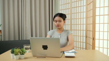 Evde oturan Asyalı bir kadın bilgisayarını kullanarak gelirini ve harcamalarını kaydediyor. Düzenli ve finansal olarak bilinçli kalıyor..