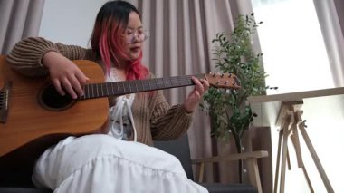 Neşeli kadın evde gitar çalarak eğleniyor. Günlük hayatta rahatlama, müzikal ifade ve yaratıcı özbakım kavramı.