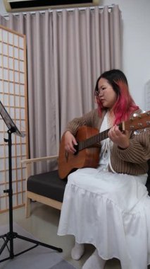 Neşeli kadın evde gitar çalarak eğleniyor. Günlük hayatta rahatlama, müzikal ifade ve yaratıcı özbakım kavramı.