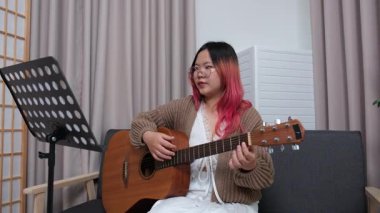 Neşeli kadın evde gitar çalarak eğleniyor. Günlük hayatta rahatlama, müzikal ifade ve yaratıcı özbakım kavramı.