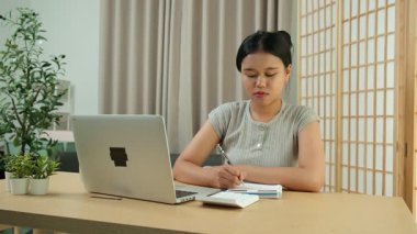 Evde oturan Asyalı bir kadın bilgisayarını kullanarak gelirini ve harcamalarını kaydediyor. Düzenli ve finansal olarak bilinçli kalıyor..