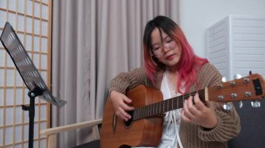 Neşeli kadın evde gitar çalarak eğleniyor. Günlük hayatta rahatlama, müzikal ifade ve yaratıcı özbakım kavramı.