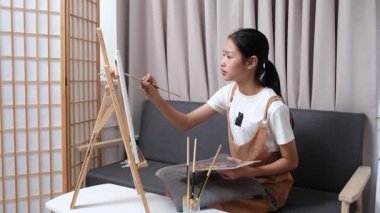 Sevimli genç kız evde resim çizerek ve boyayarak en sevdiği aktiviteyle yaratıcılığını ifade ediyor. Çocukluk hayal gücü, sanat ve oyun yoluyla öğrenme kavramı.