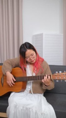 Neşeli kadın evde gitar çalarak eğleniyor. Günlük hayatta rahatlama, müzikal ifade ve yaratıcı özbakım kavramı.