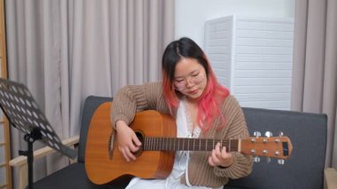 Neşeli kadın evde gitar çalarak eğleniyor. Günlük hayatta rahatlama, müzikal ifade ve yaratıcı özbakım kavramı.