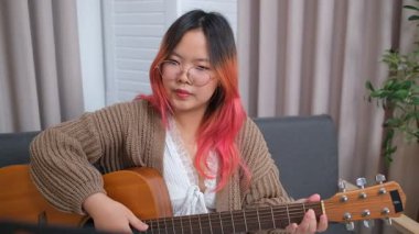 Neşeli kadın evde gitar çalarak eğleniyor. Günlük hayatta rahatlama, müzikal ifade ve yaratıcı özbakım kavramı.