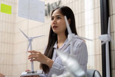 Katılımcı bir toplantıda, genç bir profesyonel, sürdürülebilirlik ve ESG ilkelerinin önemini vurgulayarak bir rüzgar türbini modeli sergileyerek yenilenebilir enerji hakkında görüşlerini paylaşıyor..