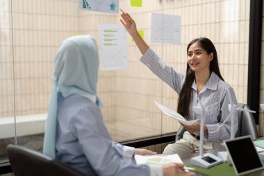 Görsel yardımları kullanan bir kadın, sürdürülebilirlik girişimleri hakkındaki fikirlerini tutkuyla sunarak, meslektaşını uygulama ve etki hakkındaki dinamik bir tartışmaya dahil ediyor..