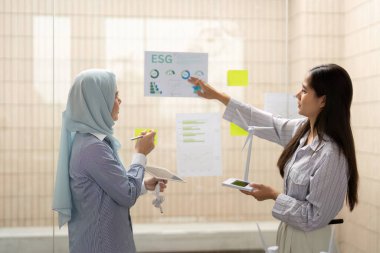 Çağdaş bir ofiste, ESG girişimleri hakkında dinamik tartışmalara giren iki kadın, sürdürülebilirliğin iş uygulamalarına entegrasyonunu vurguluyor.