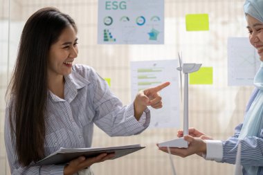 İleri görüşlü bir toplantıda, genç bir profesyonel yenilenebilir enerjinin sürdürülebilirlik ve kurumsal sorumluluk üzerindeki olumlu etkilerini göstermek için bir rüzgar türbini modeli kullanır..