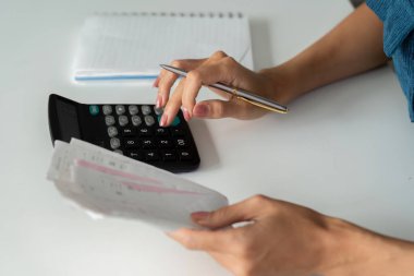 Bir birey, aylık giderlerini ve bütçelerini takip etmek için bir hesap makinesi kullanarak ve faturaları gözden geçirmeye odaklanır..