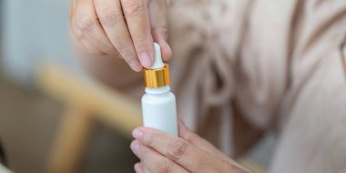 Hassasiyete odaklanan bir kadın, güzellik rutinini geliştirmek için cilt dökücü şişesinin kapağını açar..