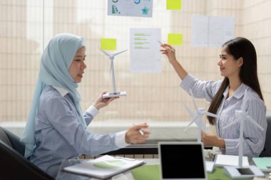 Rüzgar enerjisi modellerini gösteren iki profesyonel, etkili çevresel çözümleri sürdürülebilir uygulamaları vurgulayarak, veri görselleştirme stratejilerini tartışıyor..