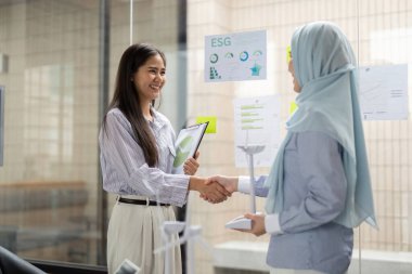 İki kadın, ESG girişimlerini ilerletme yönündeki ortak çabalarını kutlamak için bir başarı anında el sıkışıyor..