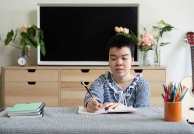 Kız aktif olarak defterine yazıyor, evde öğrenme deneyiminin tadını çıkarırken düşüncelerini ve yaratıcılığını ifade ediyor..