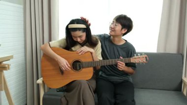 Neşeli lezbiyen çift birlikte müzik dinliyor, gitar çalıyor ve evde şarkı söylüyor. Sevgi kavramı, yaratıcılık ve duygusal bağ paylaşılan müzikal anlar.