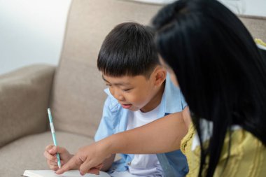 Bir anne, oğluna kişisel rehberlik ile öğrenme deneyimini geliştirmek için not defterine yazmaya odaklanırken detaylara dikkat çeker..