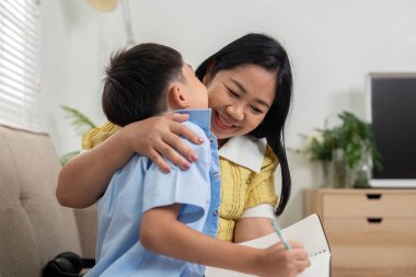 Bir anne, oğluna ev ödevlerinde yardım ederken kahkahaları ve gülümsemeleri, güçlü bir bağ ve birlikte öğrenme sevincini yansıtıyor..
