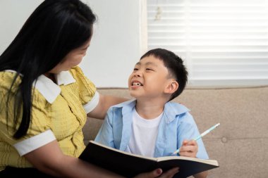 Bir anne ve oğlu, ders çalışırken bir yandan çocuk gülümserken, bir yandan da defterine yazarken keyifli bir an yaşarlar..