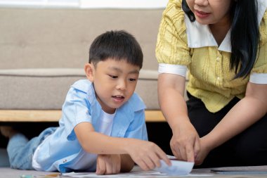 Bir çocuk, annesiyle birlikte aktif olarak yaratıcı bir öğrenme etkinliğine katılıyor. Eğitime ebeveynsel katılımın önemini vurguluyor..