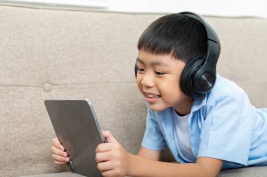 Kulaklık takan neşeli bir çocuk tabletine odaklanmış, okula dönüş sezonuna hazırlanırken kendini öğrenme aktivitelerine kaptırmış..