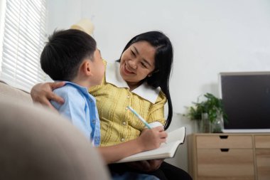 Bir anne, o ödevini yaparken oğluyla hafif bir anı paylaşır. Etkileşimleri öğrenme sevincini ve ebeveyn müdahalesinin önemini vurgular..