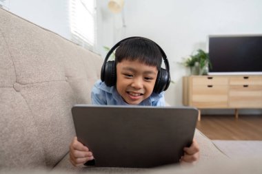 Kulaklık takan neşeli bir çocuk tabletinde interaktif öğrenmenin keyfini çıkarıyor, okula dönüş hazırlıkları ve eğitimdeki teknolojiyi gösteriyor..