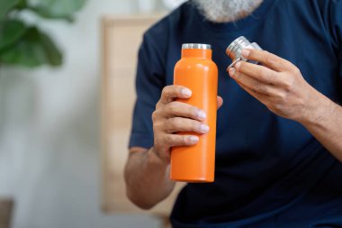 Evde portakal suyu şişesiyle su içerek sağlığa öncelik veren yaşlı bir adam sağlıklı alışkanlıkları ve farkındalığı teşvik ediyor..