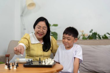 Bir anne ve oğul, sıcak bir ev ortamında satranç stratejileri öğrenirken gülücüklerini paylaşıyor, eğlence ve eğitimi ön plana çıkarıyor..