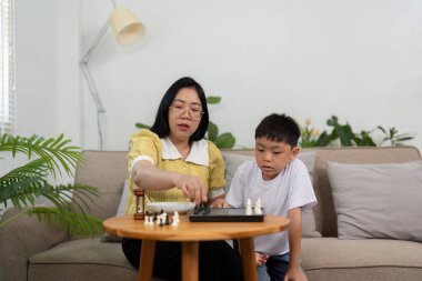 Bir anne ve oğlunun rahat bir oturma odasında satranç maçına odaklandıkları bir sahne, oyun rekabeti yoluyla ilişkilerini güçlendiriyor..